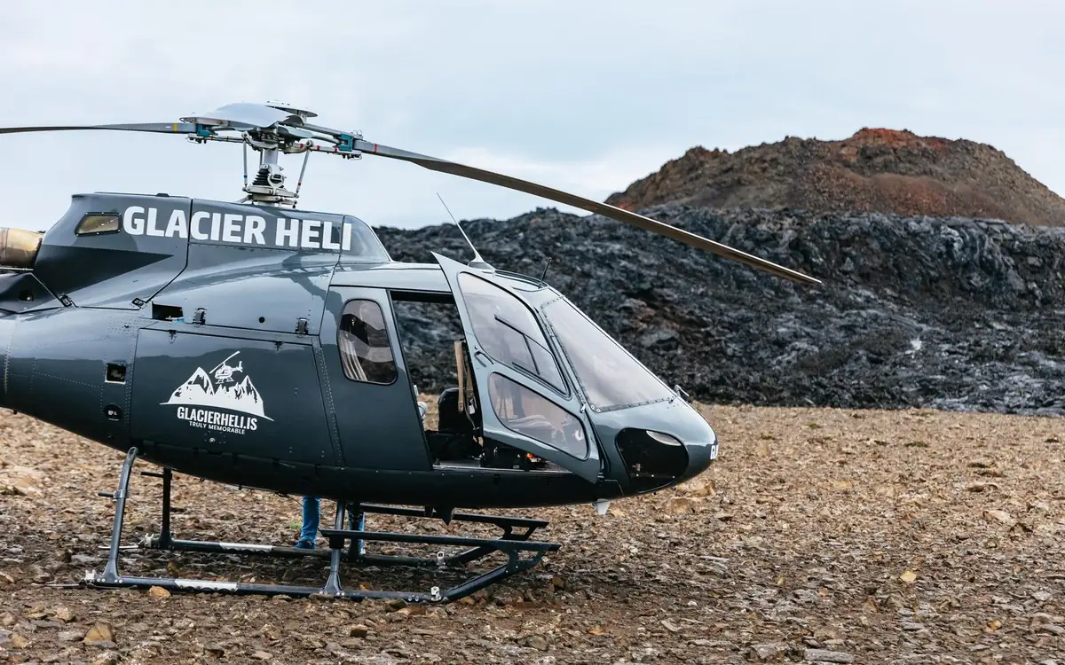 A helicopter parked on black volcanic gravel in Iceland with mountains behind