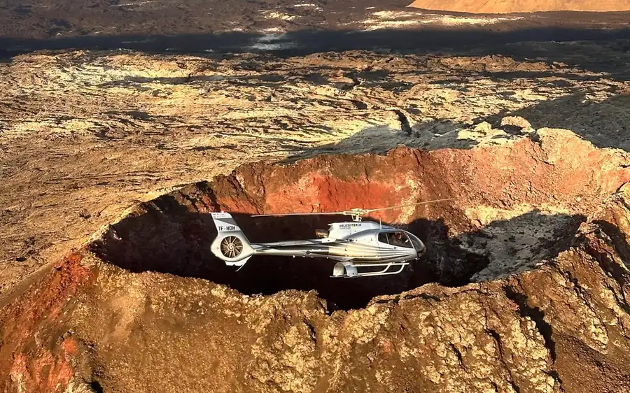 A helicopter beside a glowing eruption crater in Iceland
